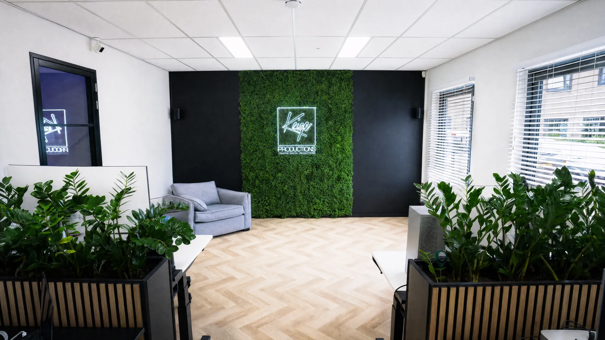 De zwarte wand met groene mosmuur en verlicht Kaige-logo, met planten op de voorgrond