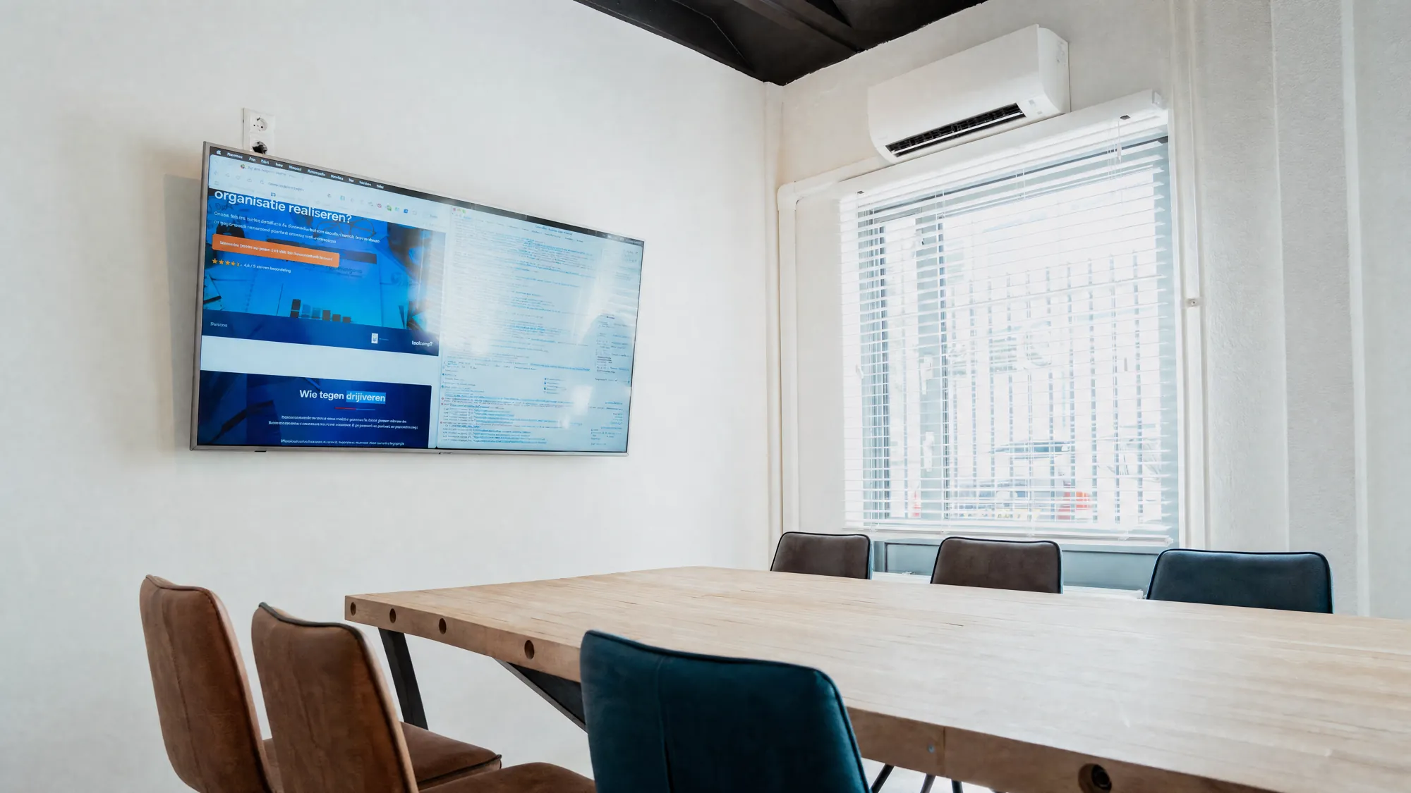 Vergaderruimte met lange houten tafel en groot scherm aan de muur